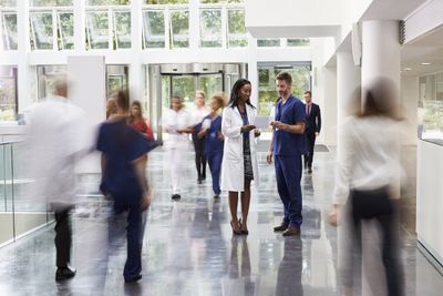 A group of people walking through a hospital lobby while two doctors talk.