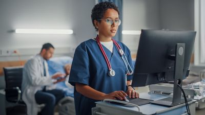 A woman in scrubs standing in front of a computer