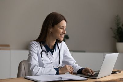 a woman in a white lab coat on her laptop