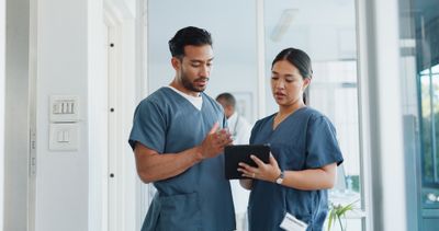 a man and woman in scrubs looking at something on a tablet