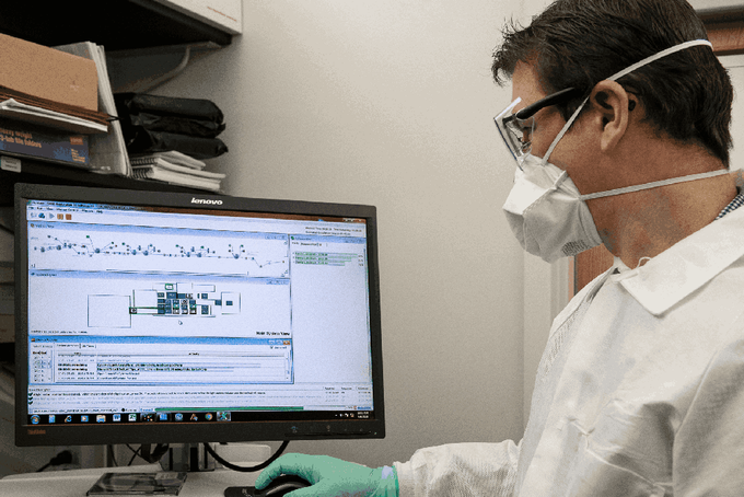 a man in a white lab coat and face mask working on a computer