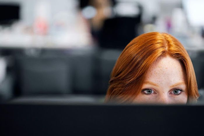 A red haired woman looking over a screen.