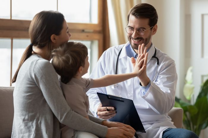 A small boy is sitting on his mother's lap and high-fiving a male doctor.