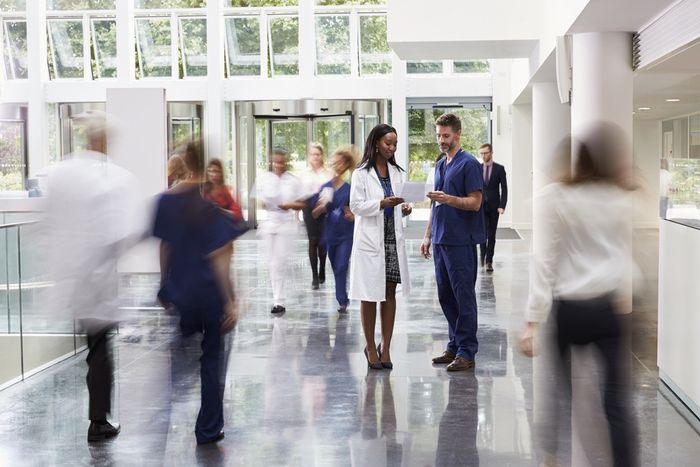 A group of people walking through a hospital lobby while two doctors talk.