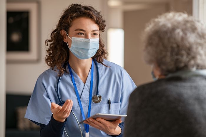 a nurse wearing a face mask talking to a patient