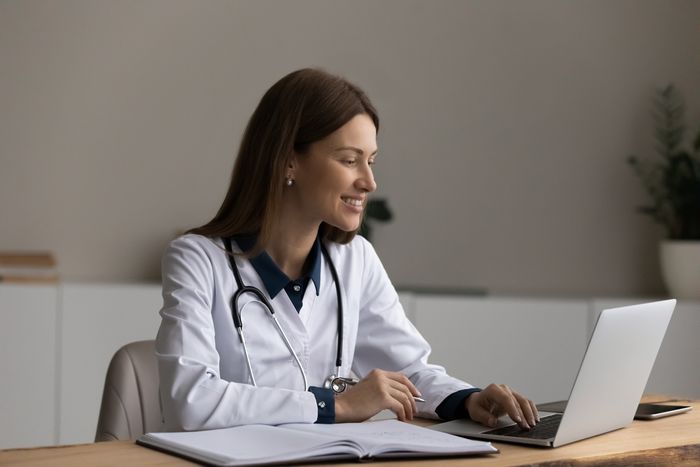 a woman in a white lab coat on her laptop