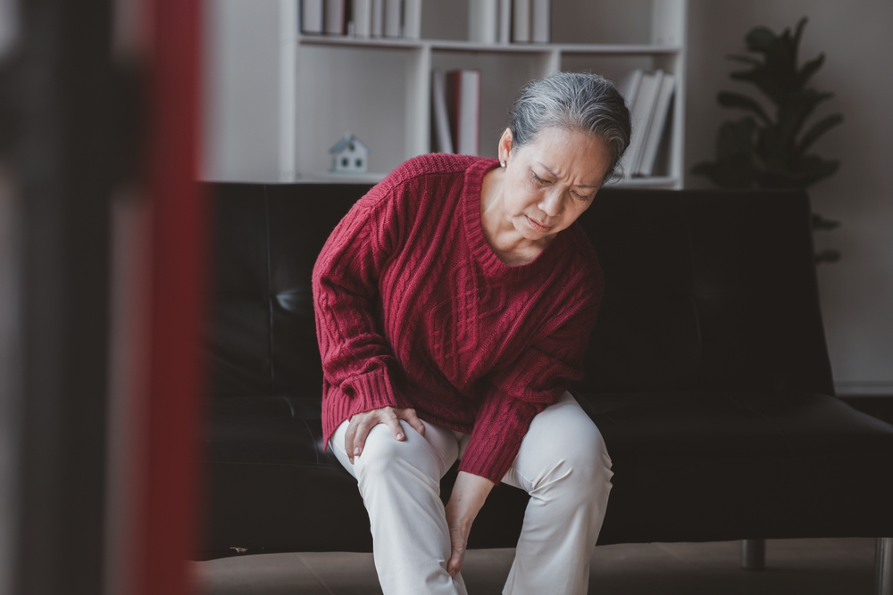 Elderly woman sitting on her couch leaning over while rubbing her legs
