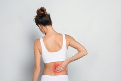 Woman putting her hand on her back from lower back pain, visibly colored red