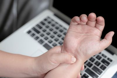 A person holding their wrist from pain caused by inflammation, in front of a laptop