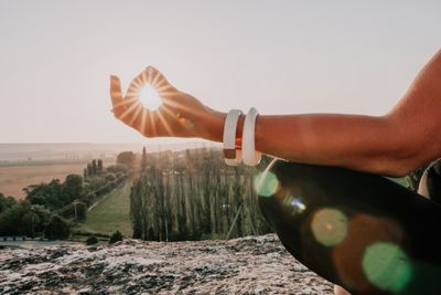 Woman meditating atop a mountain with the sun peeking through her closed fingers