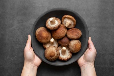 Hands holding black bowl made of clay containing Shiitake mushrooms