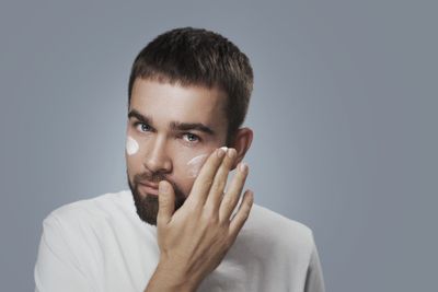 Handsome man applying anti-ageing skin cream to his cheeks