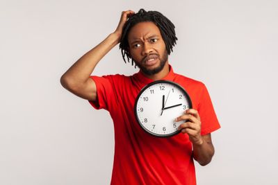 Man scratching his head holding a clock that reads 12:13