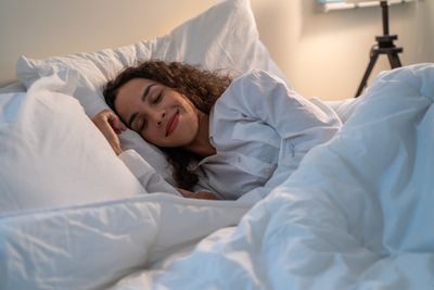 Latino woman fast asleep in bed with white sheets and pillows