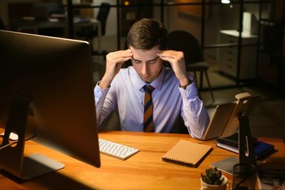 Man sitting at desk rubbing his temples with both hands
