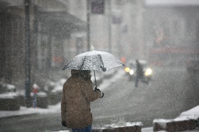 Figure in a warm jacket under an umbrella walking outside in light snow