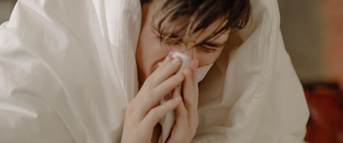 Sick individual wrapped in blankets blowing his nose in tissue paper