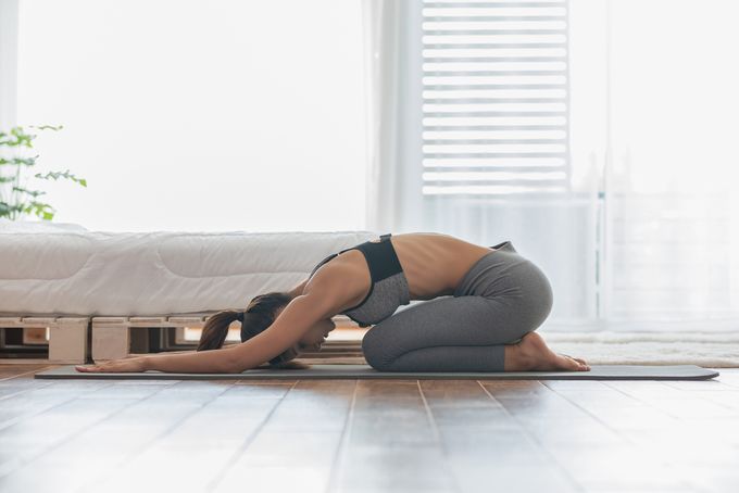 Woman in yoga clothing performing Child's Pose on a yoga matt in her living room