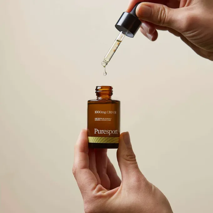A person measuring out a dosage of CBD oil from a bottle of Puresport 