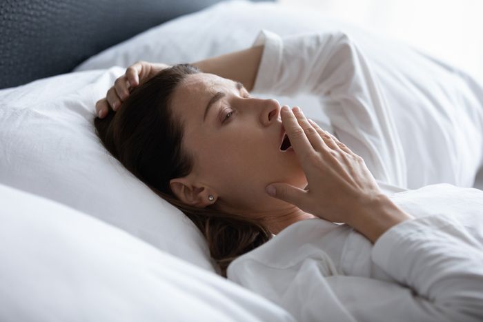 Woman lying in bed yawning after a sleepless nights as if not having gotten enough hours of sleep