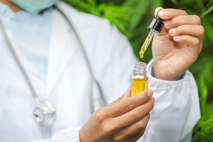Doctor in lab coat measuring out a dosage of CBD drops with a dropper