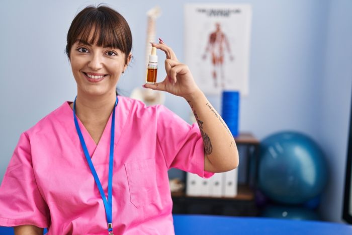 A nurse in a pink shirt holding up a bottle of CBD oil intended to treat pain