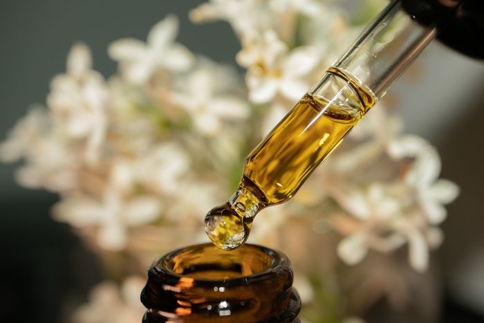 A glass bottle and dropper filled with CBD oil in front of a white flower