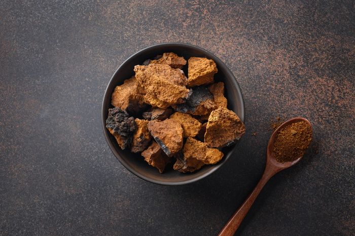 Raw dried Chaga mushrooms in a bowl next to a spoon of powdered Chaga extract