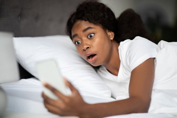 Young woman waking up and checking her phone in shock