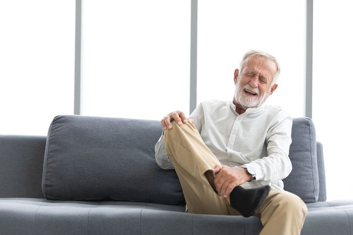 Older male holding knee and shin with pained look on face