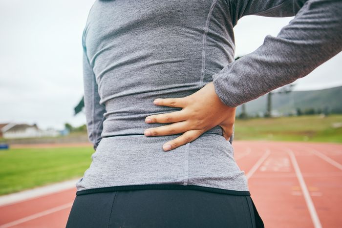 Woman clutching her back mid-race on an athletics track due to lower back pain.