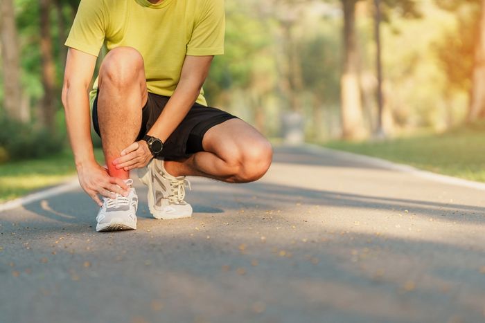 Man in the middle of running hunched over and grasping his ankle due to musculoskeletal pain