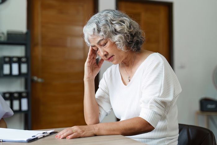 Elderly woman leaning over on table rubbing her temples while dealing with stress