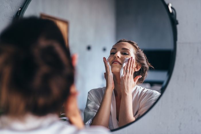 Woman smiling in the bathroom mirror while rubbing Turkey Tail mushroom-infused skincare products on her cheeks