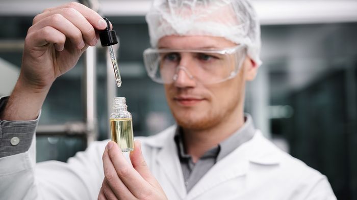 A pharmacist in a lab coat holding a dropper and bottle of vegan CBD oil