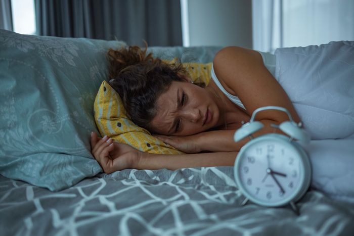 Woman with sleep anxiety lying in bed afraid to fall asleep next to an alarm clock