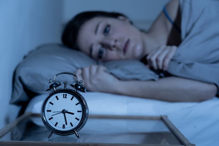 Woman lying in bed at night awake with anxiety and sleep disturbance with an alarm clock next to her