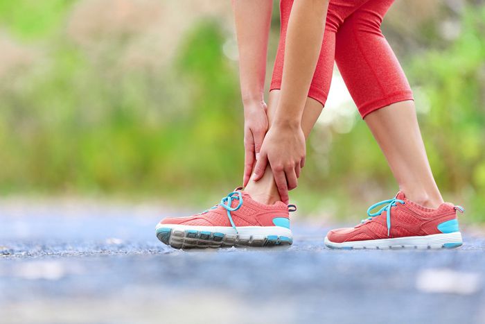 Close-up of woman's legs while holding her ankles suggesting inner ankle pain