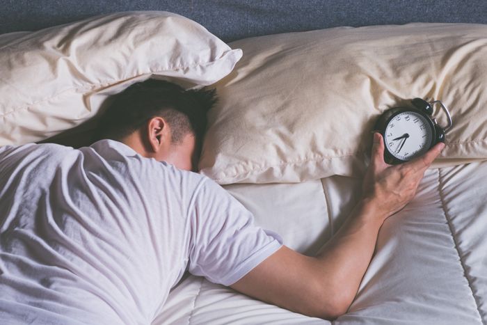 Man suffering from parasomnia lying in the bed tired holding an alarm clock