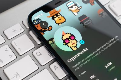 Close-up of a phone screen showing official CryptoPunks page with a computer keyboard behind it.