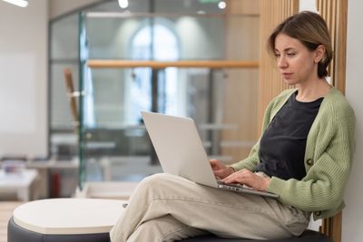 A young woman seated with one leg crossed over the other, working on her laptop.