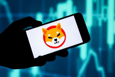 A person holding their smartphone, with the Shiba Inu Token displayed on the screen against a white background, with heat maps visible in the background of the image.
