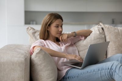 A woman seated comfortably on a couch in her living room, busy working on her laptop.