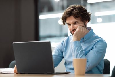 Shopify seller sitting in front of his laptop computer with a cup of coffee looking confused while he tries to hide Shopify products