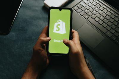 a person holding a cell phone with a Shopify logo on the screen