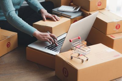 Shopify seller sitting on the floor working on a laptop surrounded by boxes