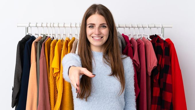 a woman pointing at a rack of clothes