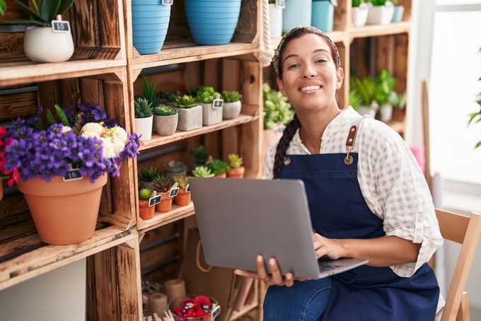 Florist holding laptop next to shelf of plants