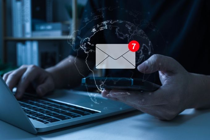 A person using a cell phone and a laptop receiving email notifications for back-in-stock products