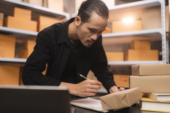 Shopify store owner using product handles while checking stock with boxes on shelves behind him